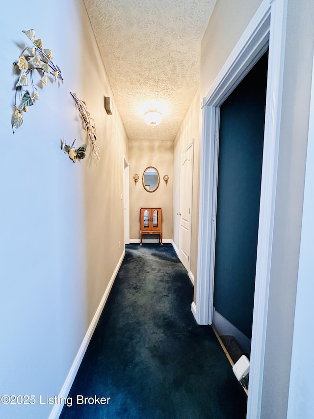 corridor with a textured ceiling and dark colored carpet