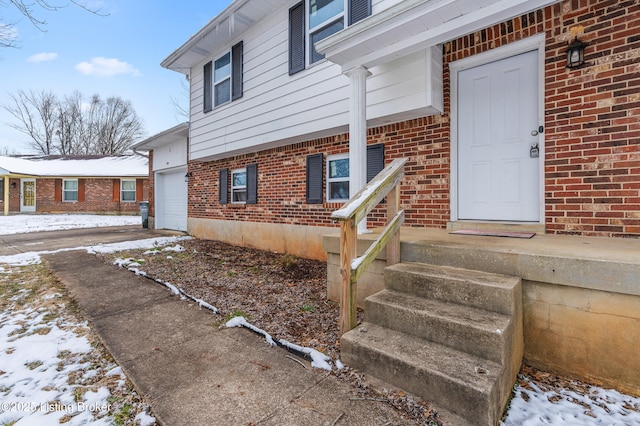 snow covered property entrance with brick siding and an attached garage