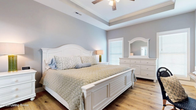 bedroom with a tray ceiling, visible vents, light wood-style flooring, ornamental molding, and multiple windows