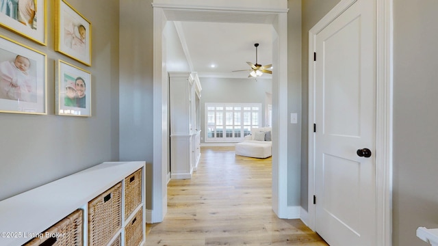 hall with light wood-type flooring, visible vents, ornamental molding, and baseboards