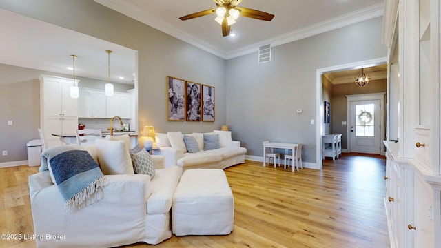 living area featuring light wood finished floors, baseboards, visible vents, and crown molding