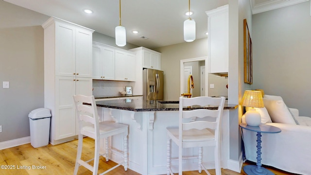 kitchen featuring stainless steel fridge, a breakfast bar, a peninsula, light wood-style floors, and white cabinetry