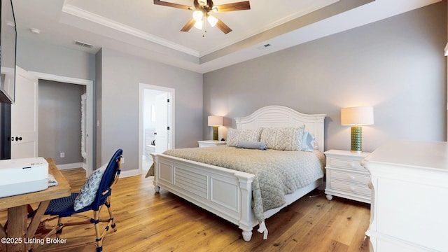 bedroom with light wood finished floors, visible vents, a raised ceiling, baseboards, and ornamental molding