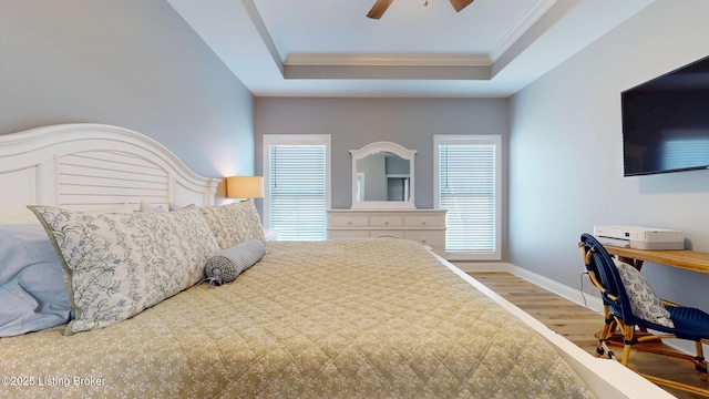 bedroom featuring baseboards, ceiling fan, ornamental molding, wood finished floors, and a tray ceiling