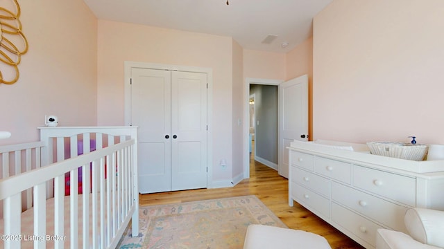 bedroom featuring a crib, light wood-style flooring, baseboards, and a closet