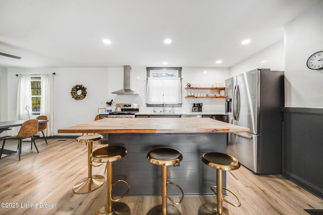 4708 S 3rd St, Louisville, KY 40214 - kitchen with butcher block countertops, appliances with stainless steel finishes, wall chimney range hood, light wood-style flooring, and a kitchen breakfast bar