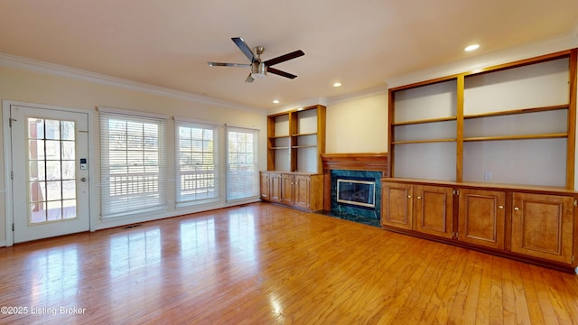 unfurnished living room featuring a high end fireplace, ceiling fan, light hardwood / wood-style floors, crown molding, and built in shelves