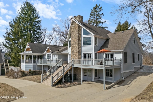 view of front of house with driveway, french doors, stairway, a wooden deck, and a chimney