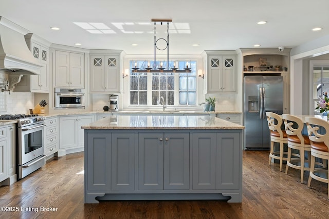 kitchen featuring a center island, decorative light fixtures, custom exhaust hood, appliances with stainless steel finishes, and glass insert cabinets