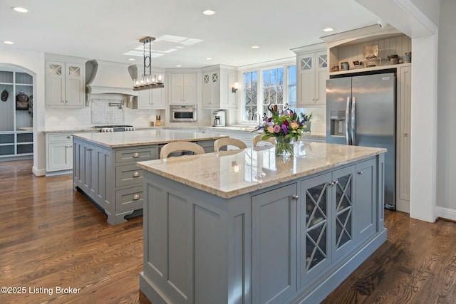 kitchen with a large island, appliances with stainless steel finishes, glass insert cabinets, hanging light fixtures, and premium range hood