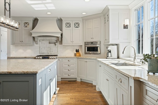 kitchen featuring a sink, stainless steel oven, wall chimney range hood, light stone countertops, and pendant lighting