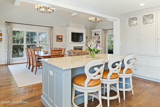 kitchen with light stone countertops, dark wood-style flooring, a notable chandelier, and a center island