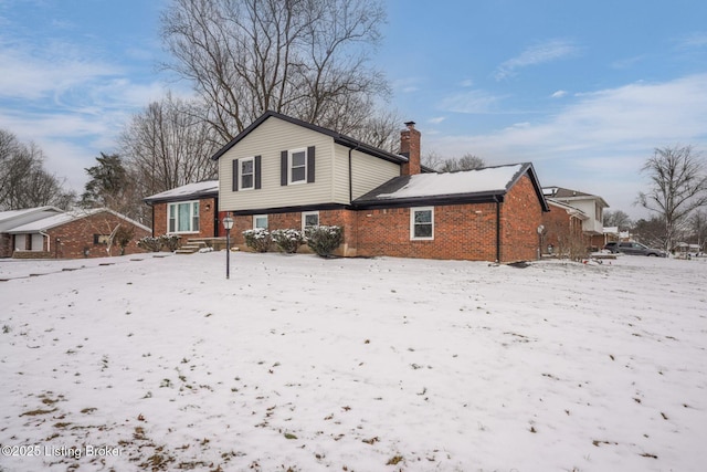 snow covered property featuring a chimney and brick siding