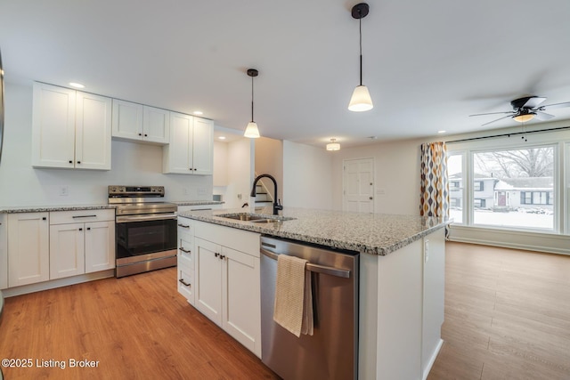 kitchen with hanging light fixtures, light wood-style flooring, appliances with stainless steel finishes, white cabinets, and a sink