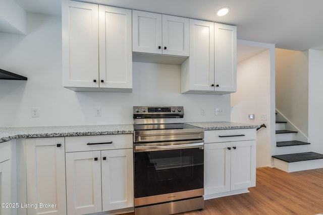 kitchen featuring light stone countertops, light wood finished floors, white cabinetry, and stainless steel electric stove