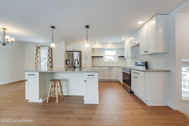 kitchen featuring stainless steel appliances, a breakfast bar, white cabinets, light wood finished floors, and a center island with sink