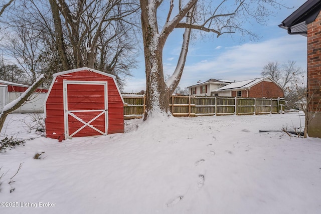 snow covered structure featuring an outbuilding, fence, and a storage unit