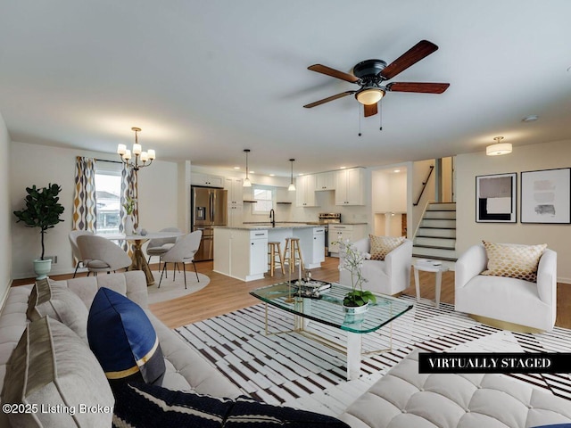 living area featuring light wood-style floors, ceiling fan with notable chandelier, and stairs