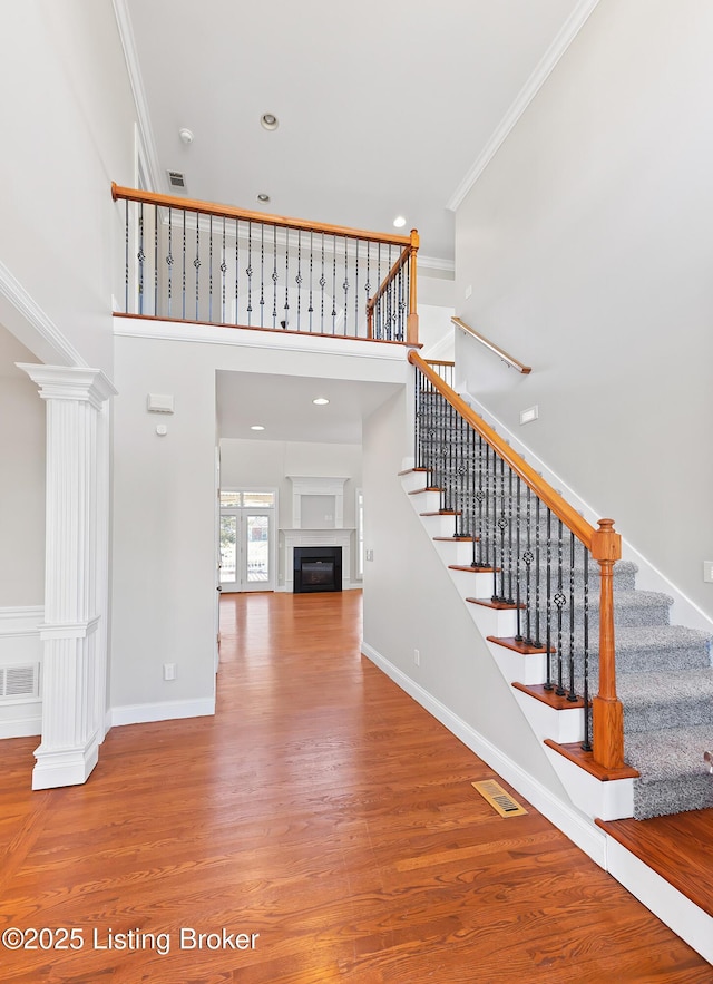 stairs featuring hardwood / wood-style flooring, ornamental molding, decorative columns, and a towering ceiling