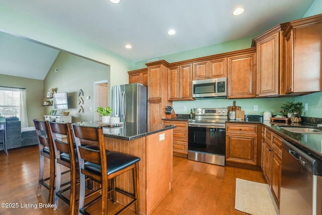 kitchen with stainless steel appliances, light hardwood / wood-style floors, vaulted ceiling, a kitchen island, and a kitchen bar