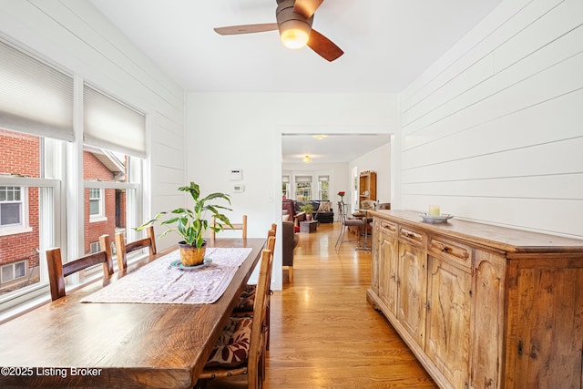 dining space featuring wooden walls, ceiling fan, and light hardwood / wood-style flooring