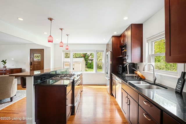 kitchen featuring a kitchen bar, sink, hanging light fixtures, light hardwood / wood-style flooring, and appliances with stainless steel finishes