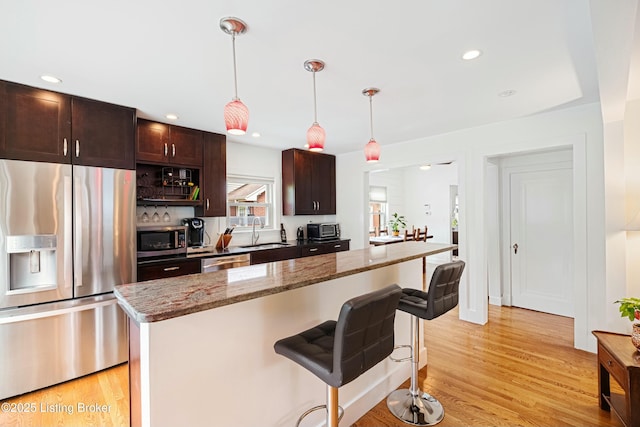 kitchen with sink, light stone counters, a center island, pendant lighting, and stainless steel appliances