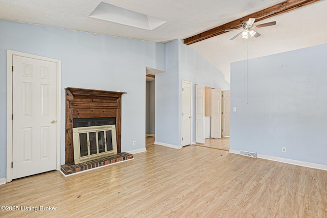 unfurnished living room featuring a brick fireplace, light hardwood / wood-style floors, vaulted ceiling with beams, and ceiling fan