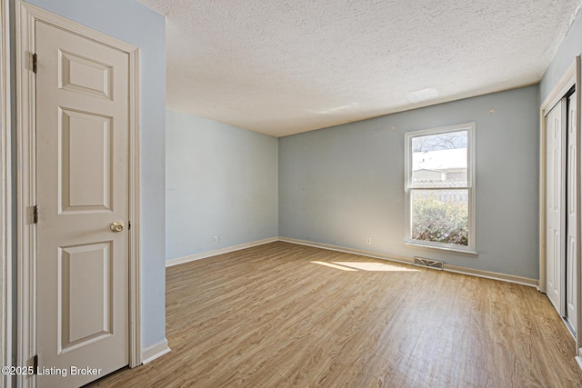 unfurnished room with light wood-type flooring and a textured ceiling