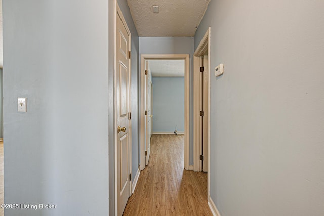 hallway with light hardwood / wood-style floors and a textured ceiling