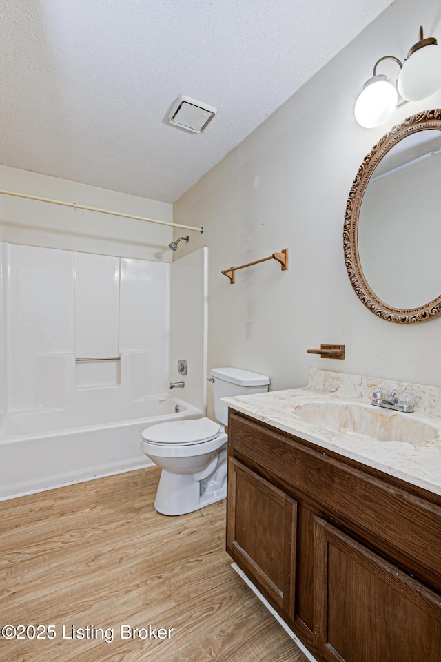 full bathroom featuring hardwood / wood-style flooring, toilet, a textured ceiling, washtub / shower combination, and vanity