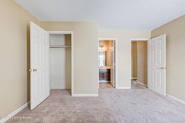 unfurnished bedroom featuring connected bathroom, a closet, light carpet, and a textured ceiling