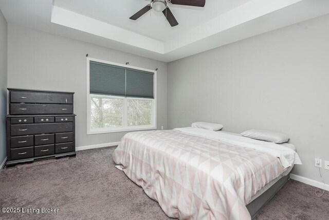 bedroom with a ceiling fan, a tray ceiling, baseboards, and dark colored carpet