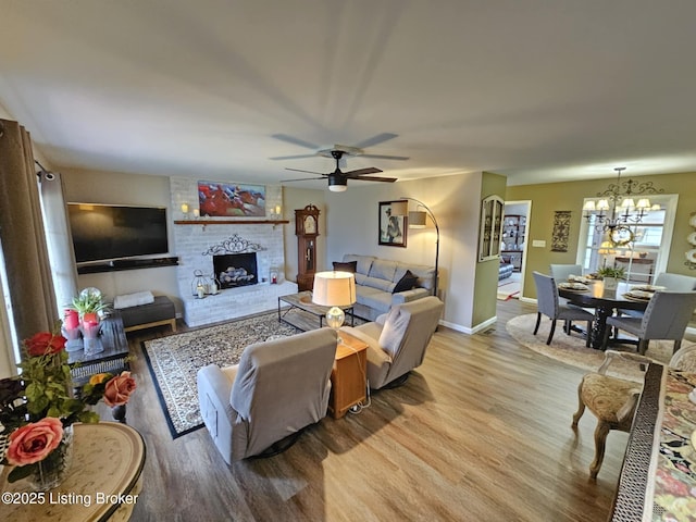 living room featuring a brick fireplace, ceiling fan with notable chandelier, and light hardwood / wood-style flooring