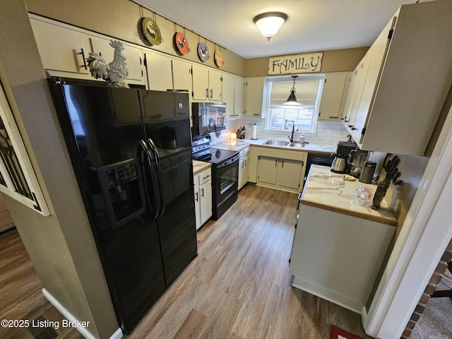 kitchen featuring decorative light fixtures, sink, decorative backsplash, black appliances, and light hardwood / wood-style flooring