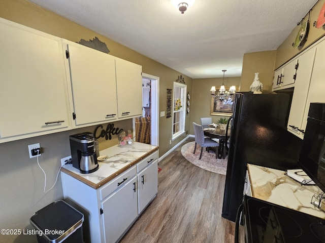 kitchen featuring hardwood / wood-style floors, decorative light fixtures, white cabinetry, a notable chandelier, and black appliances