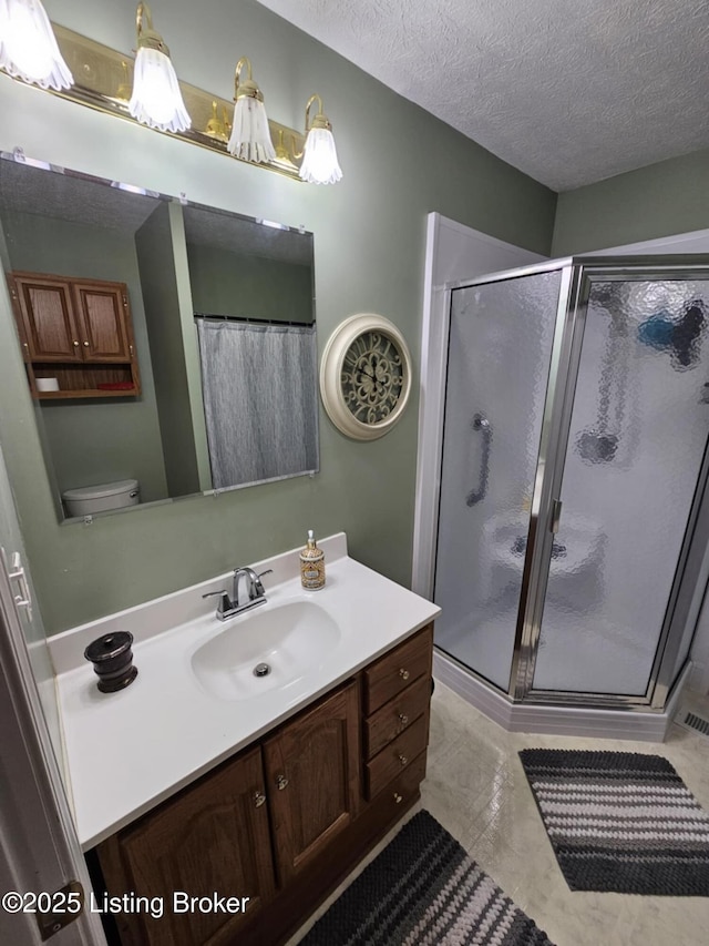 bathroom featuring vanity, toilet, a shower with shower door, and a textured ceiling