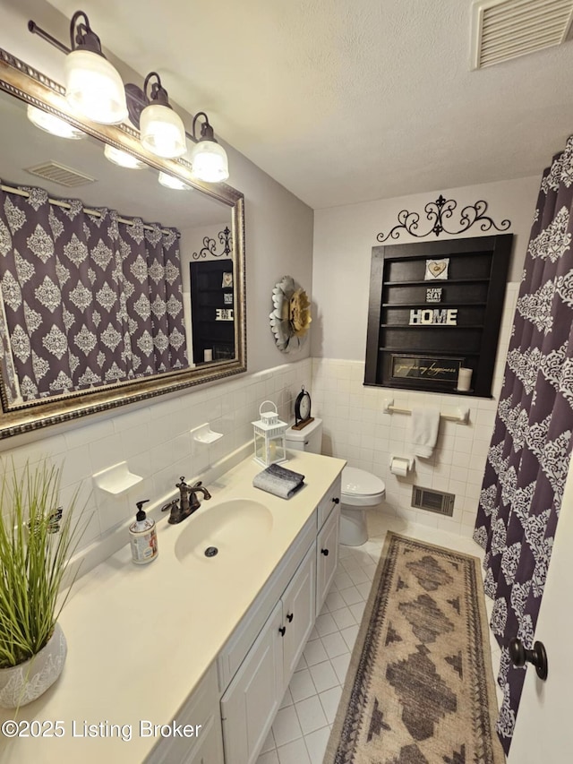 bathroom featuring tile patterned flooring, tile walls, vanity, a textured ceiling, and toilet