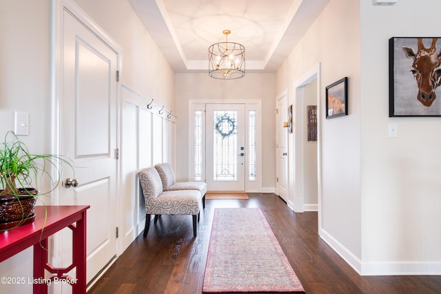 entryway with dark wood-style flooring, an inviting chandelier, a raised ceiling, and baseboards