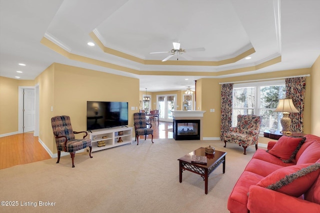 carpeted living area featuring a ceiling fan, baseboards, a tray ceiling, recessed lighting, and crown molding