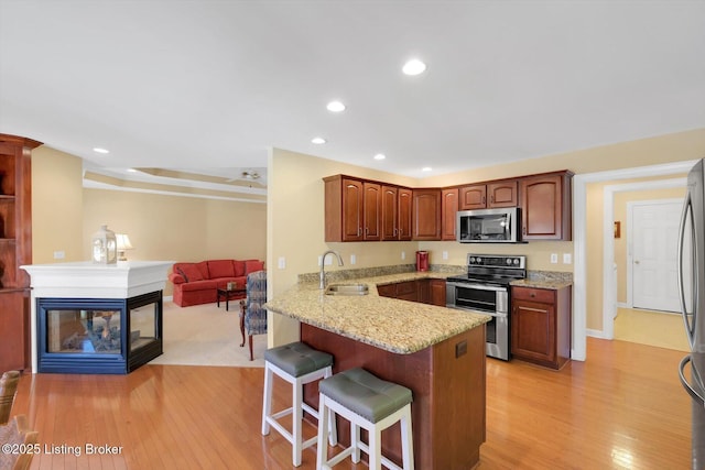 kitchen featuring light stone countertops, a kitchen breakfast bar, appliances with stainless steel finishes, a peninsula, and a sink