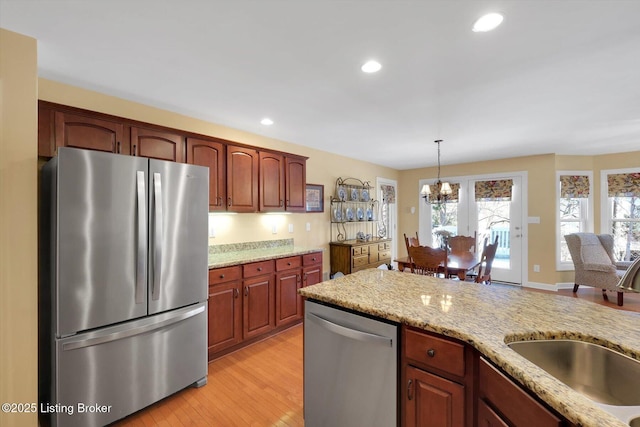 kitchen featuring a sink, decorative light fixtures, stainless steel appliances, an inviting chandelier, and light stone countertops