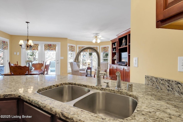 kitchen featuring ceiling fan with notable chandelier, hanging light fixtures, light stone countertops, and a sink