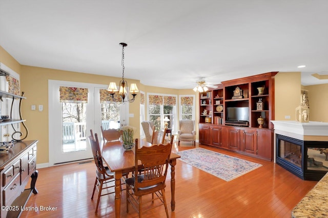 dining room with a multi sided fireplace, visible vents, light wood-style flooring, and ceiling fan with notable chandelier