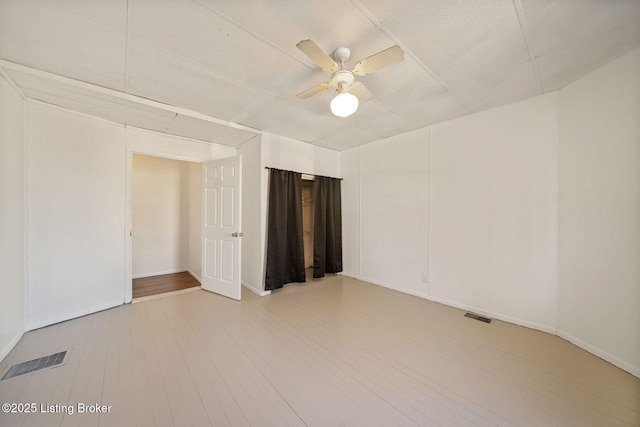 unfurnished room with ceiling fan, light wood finished floors, visible vents, and baseboards
