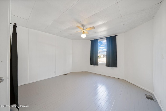 unfurnished room featuring a paneled ceiling, visible vents, ceiling fan, wood finished floors, and baseboards