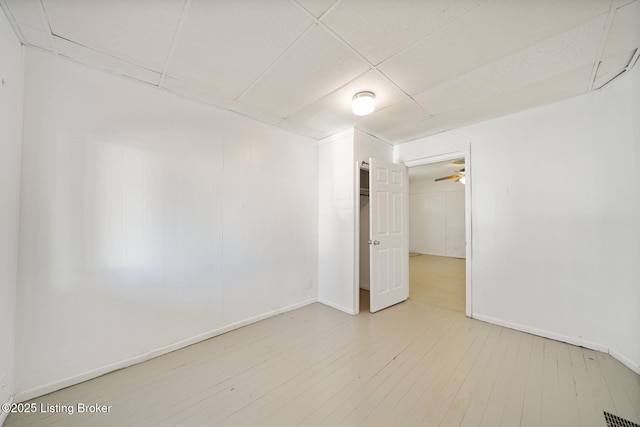 spare room featuring a paneled ceiling, visible vents, a ceiling fan, wood finished floors, and baseboards