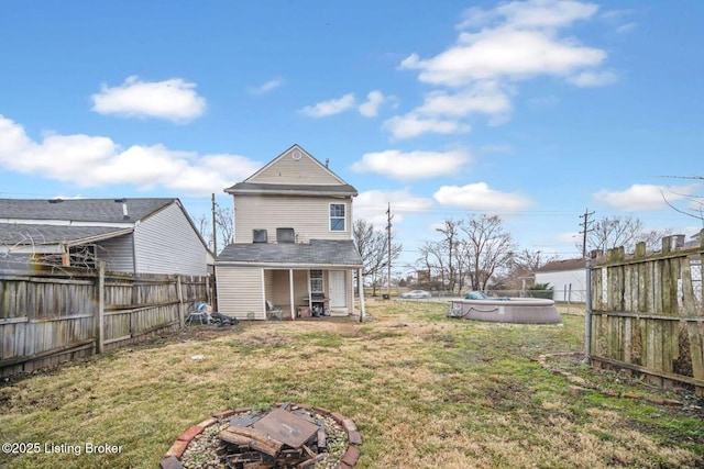 back of property featuring an outdoor fire pit, a fenced backyard, a fenced in pool, and a lawn