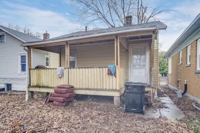 entrance to property featuring covered porch, roof with shingles, and a chimney