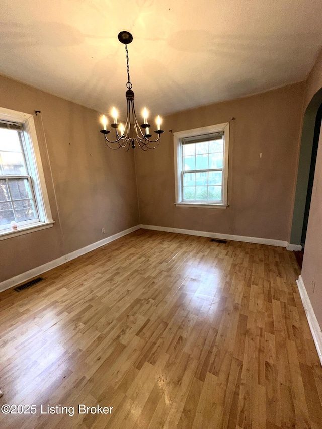 empty room featuring baseboards, visible vents, arched walkways, wood finished floors, and a notable chandelier